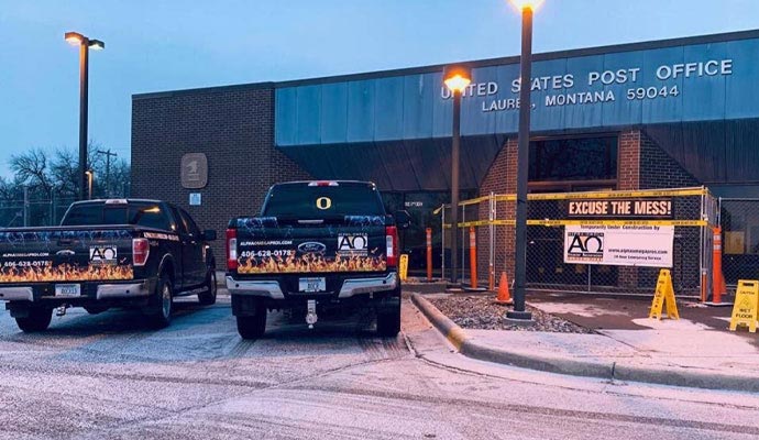 Two Alpha Omega Disaster Restoration trucks parked in front of the United States Post Office in Laurel, Montana