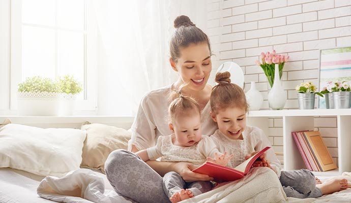 A mother sitting on a bed and reading a book with her two young daughters